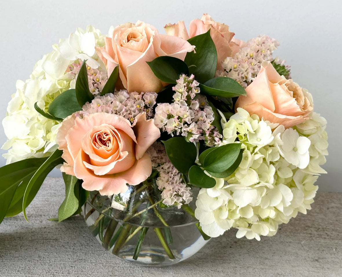 Peach low round centrepiece with roses hydrangea and statice for wedding or event