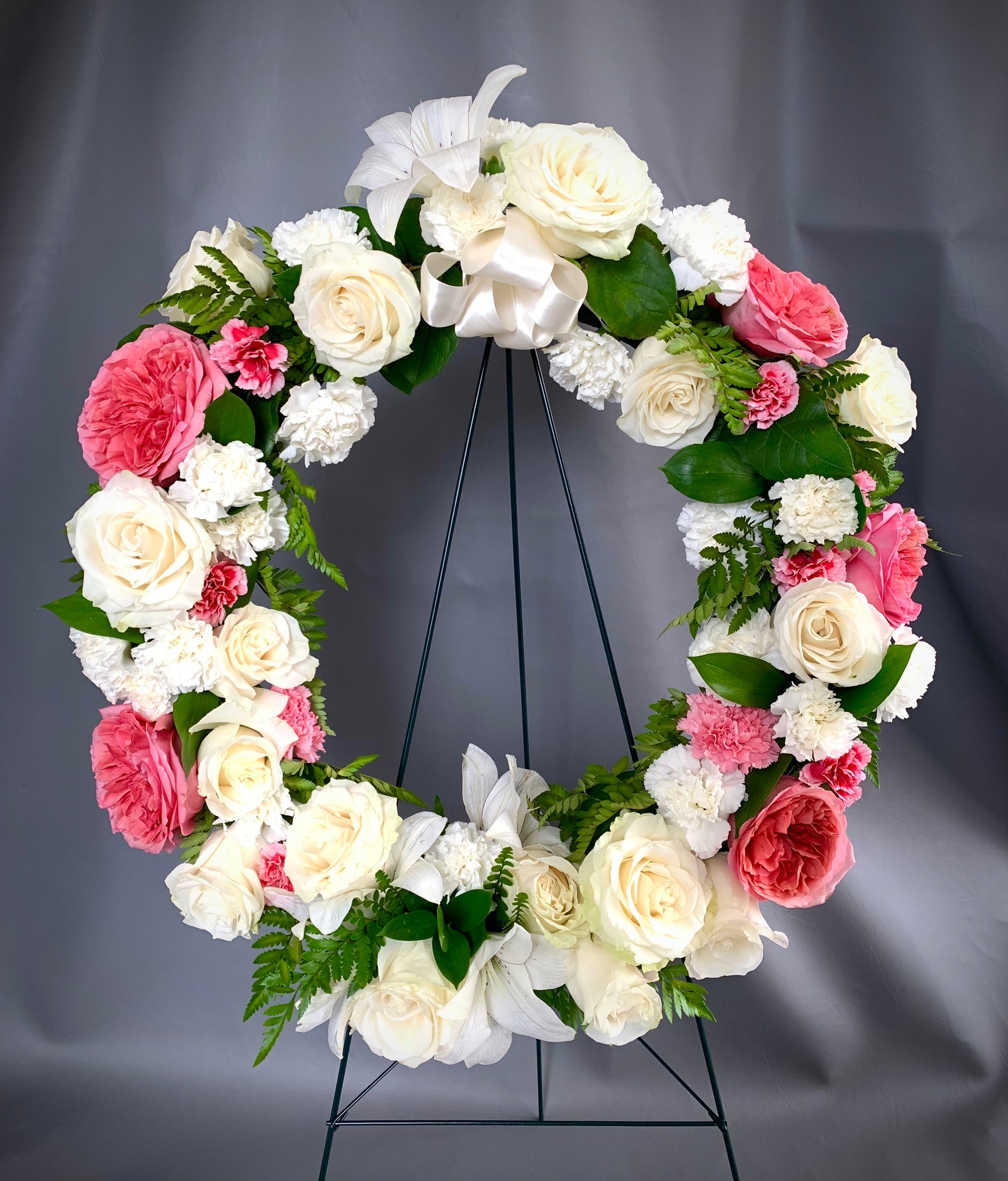 A gentle tribute to your loved one, this delicate fresh floral wreath features pink and white roses, white lilies and pink and white carnations. A ribbon and easel are included. Next day deliver to the location of your choice, funeral home or ceremony venue. Message us to customize colours, and add a personalized message card.